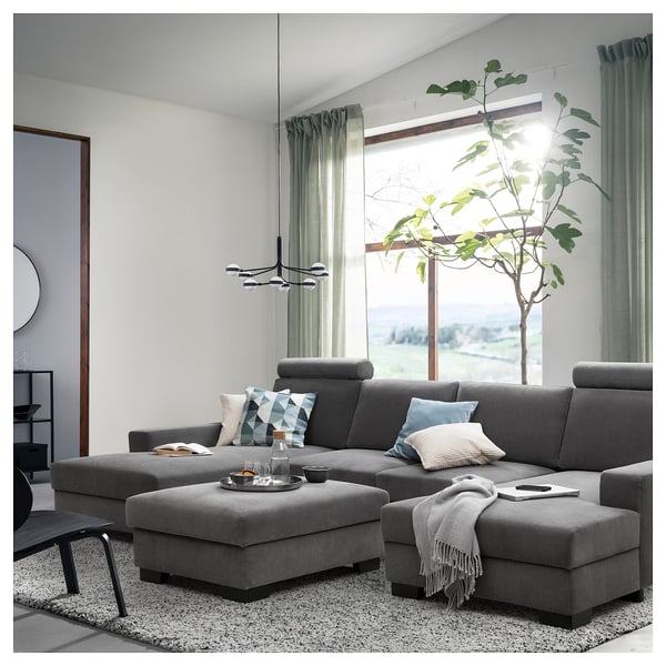 Modernes Wohnzimmer mit grauer SÖRVALLEN-Sofagarnitur, großem Fenster, grünen Vorhängen und einer hohen Pflanze.