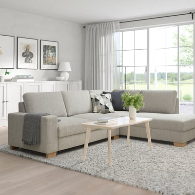Modernes Wohnzimmer mit grauem SÖRVALLEN-Sofa. Heller Couchtisch aus Holz, weißer Teppich, große Fenster, sanfte Beleuchtung. Minimalistischer skandinavischer Stil.