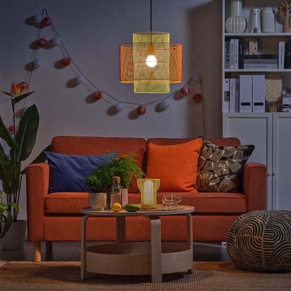 Orangefarbenes Sofa, Kissen, Couchtisch, Lichterketten, Pflanze, Dekor.
