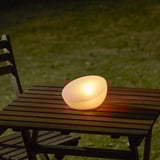 Eine kleine, leuchtende Solarlampe sitzt auf einer Holzbank. Er leuchtet nachts automatisch auf und wird durch Sonnenlicht versorgt.