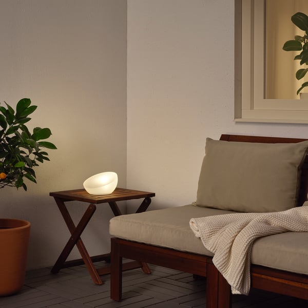 SOLVINDEN Lampe auf Holztisch, weiches Licht abstrahlend neben gepolsterter Bank mit Decke, an beiger Wand mit Spiegel.