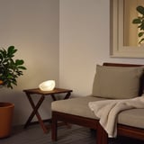 SOLVINDEN Lampe auf Holztisch, weiches Licht abstrahlend neben gepolsterter Bank mit Decke, an beiger Wand mit Spiegel.