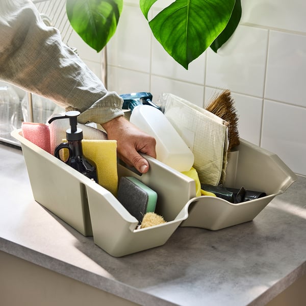 Person, die einen mit Schwämmen, Seifenspender und Bürsten gefüllten SORTERA-Vorratsbehälter auf einer Arbeitsplatte hält.