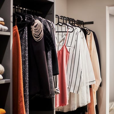 Ein Kleiderschrank mit Kleiderbügeln auf Kleiderbügeln, mit platzsparenden SPRUTTIG Kleiderbügeln in Schwarz, der vielen Outfits gut passt.