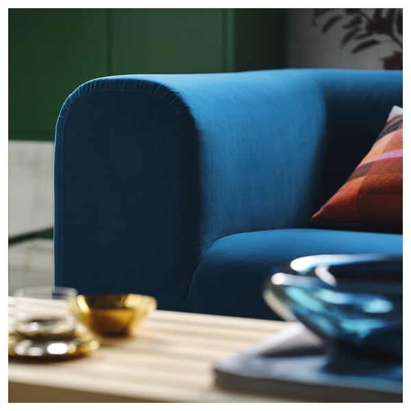 Ein leuchtend blaues Sofa mit Plüschkissen, das hochwertiges Design und Komfort ausstrahlt, in der Nähe eines Holztisches mit Dekorationsgegenständen.