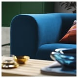 Ein leuchtend blaues Sofa mit Plüschkissen, das hochwertiges Design und Komfort ausstrahlt, in der Nähe eines Holztisches mit Dekorationsgegenständen.