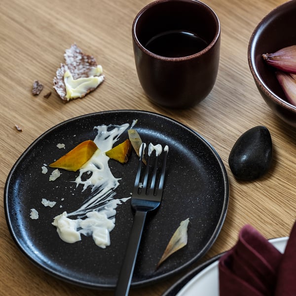 Leerer Teller mit Gabel, Kuchenreste und eine Kaffeetasse auf Holztisch.