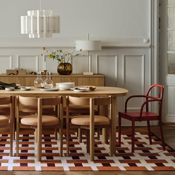 Modernes Esszimmer mit ovalem Holztisch, sechs Stühlen, buntem Teppich und Pendelleuchte.