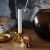 Goldene Kerzenständer auf einem Holztisch. Einer hält eine weiße Kerze in der Hand, die Rauch ausstößt.