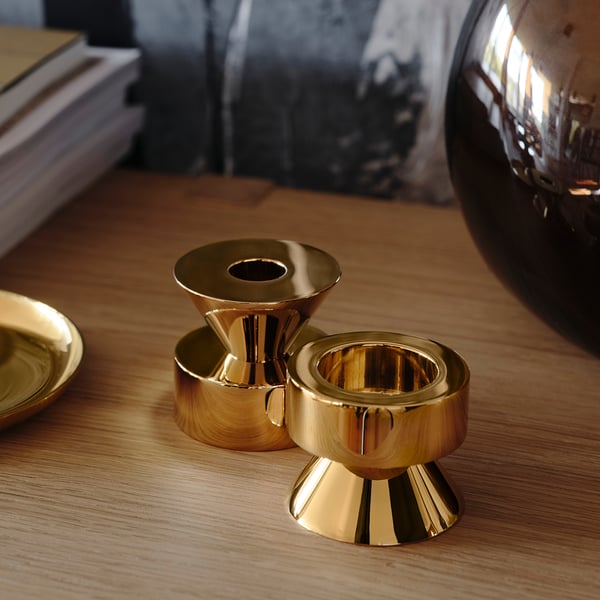 Drei goldene Kerzenständer, zwei stehende, einer liegende, poliertes Metall auf Holztisch.
