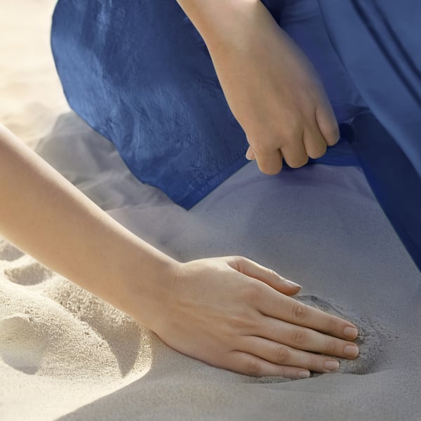 Kinderhand greift nach Erwachsenenhand am Sandstrand unter blauem Stoffschutz.