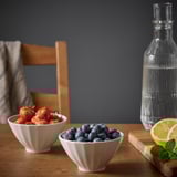 Zwei weiße Keramikschalen gefüllt mit Erdbeeren und Heidelbeeren auf einem Holztisch, mit Flasche und Zitronenscheibe in der Nähe.