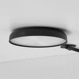 Moderne schwarze Deckenleuchte teilweise sichtbar, montiert an einer weißen Wand. Strahlt ein helles, gleichmäßiges Leuchten aus.