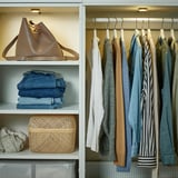 Organisierter Kleiderschrank mit beleuchteten Regalen. Die Kleidung hängt ordentlich auf der rechten Seite, die gefaltete Jeans stapelt sich unter der großen beigen Handtasche, ein zusätzlicher Weidenkorb auf dem niedrigen Regal.