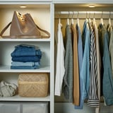 Organisierter Kleiderschrank mit Kleidung und Accessoires. Spotlight beleuchtet Regale mit einer großen Handtasche, gefalteten Jeans und einem geflochtenen Korb.