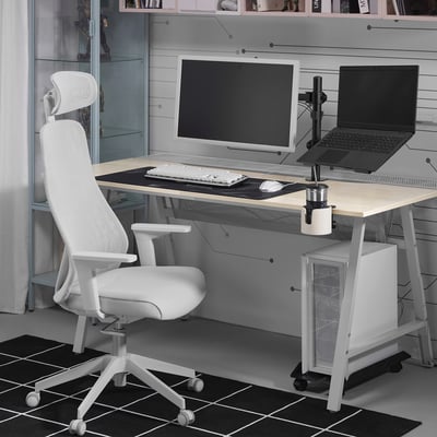 Minimalistisches Homeoffice: STUBBERGET Laptopständer, Schreibtischstuhl, Monitor, Tastatur, Tischset und Tasse auf grauem Schreibtisch; Bücherregal, Fenster.