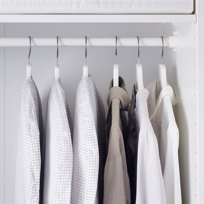 Weißer Schrank mit drei grau karierten Kleiderbezügen, die die Kleidungsstücke vor Staub schützen.