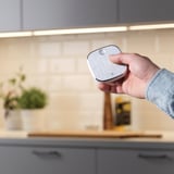 Hand mit STYRBAR-Fernbedienung in der Küche, Steuerung des intelligenten Lichts. Finish aus gebürstetem Stahl, einfaches Design für einfache Bedienung.