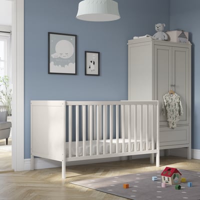 SUNDVIK weißes Babybett in der Nähe des grauen Kleiderschranks, blaue Wand mit Spielzeug und Postern.