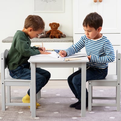 Zwei Kinder sitzen an einem kleinen weißen Tisch und zeichnen mit Buntstiften.