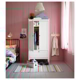 Kinderzimmer mit weißem SUNDVIK-Kleiderschrank, Bär, Kleidung, Teppich, rosa Wänden, schwarzem Bett, Lampe, Postern und Vorhang.
