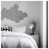 Modernes, minimalistisches Schlafzimmer mit weißer Bettwäsche, schwarzer Lampe auf weißem Nachttisch und grauer kreisförmiger Wanddekoration.