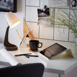 Moderner Arbeitsplatz mit weißem Schreibtisch, schwarzer Tasse, Tablet, Lampe, Stiften und Pflanze.