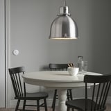 SVARTNORA Lampe, schlanke gewölbte Pendelleuchte über dem Esstisch mit schwarzen Stühlen, großes silbernes Brennlicht.