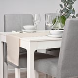 Weißer Esstisch mit grauen Stühlen; Set mit Schalen, Tellern, Weingläsern und grüner Vase mit Pflanze.