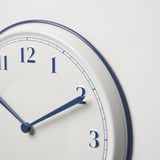Moderne Wanduhr mit weißem Zifferblatt, blauen Akzenten und großen Ziffern; zeigt die Zeit mit 2:07 an.