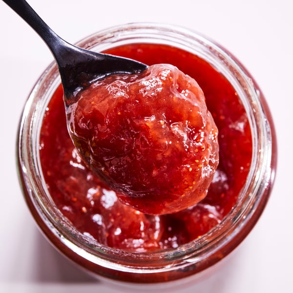 Ein Glas leuchtend rote Erdbeermarmelade mit einem Löffel voll herausgehobenem Glas.