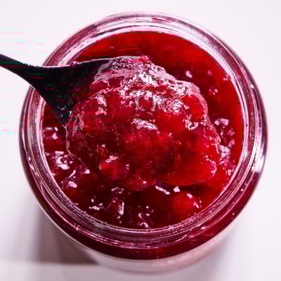 Offenes Glas mit leuchtend roter Preiselbeermarmelade, Löffel voll angehoben, Glasbehälter.