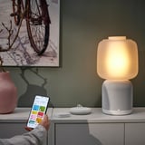 Hand hält das Smartphone, um die beleuchtete SYMFONISK-Lampe über die ikea home smart App zu steuern.
