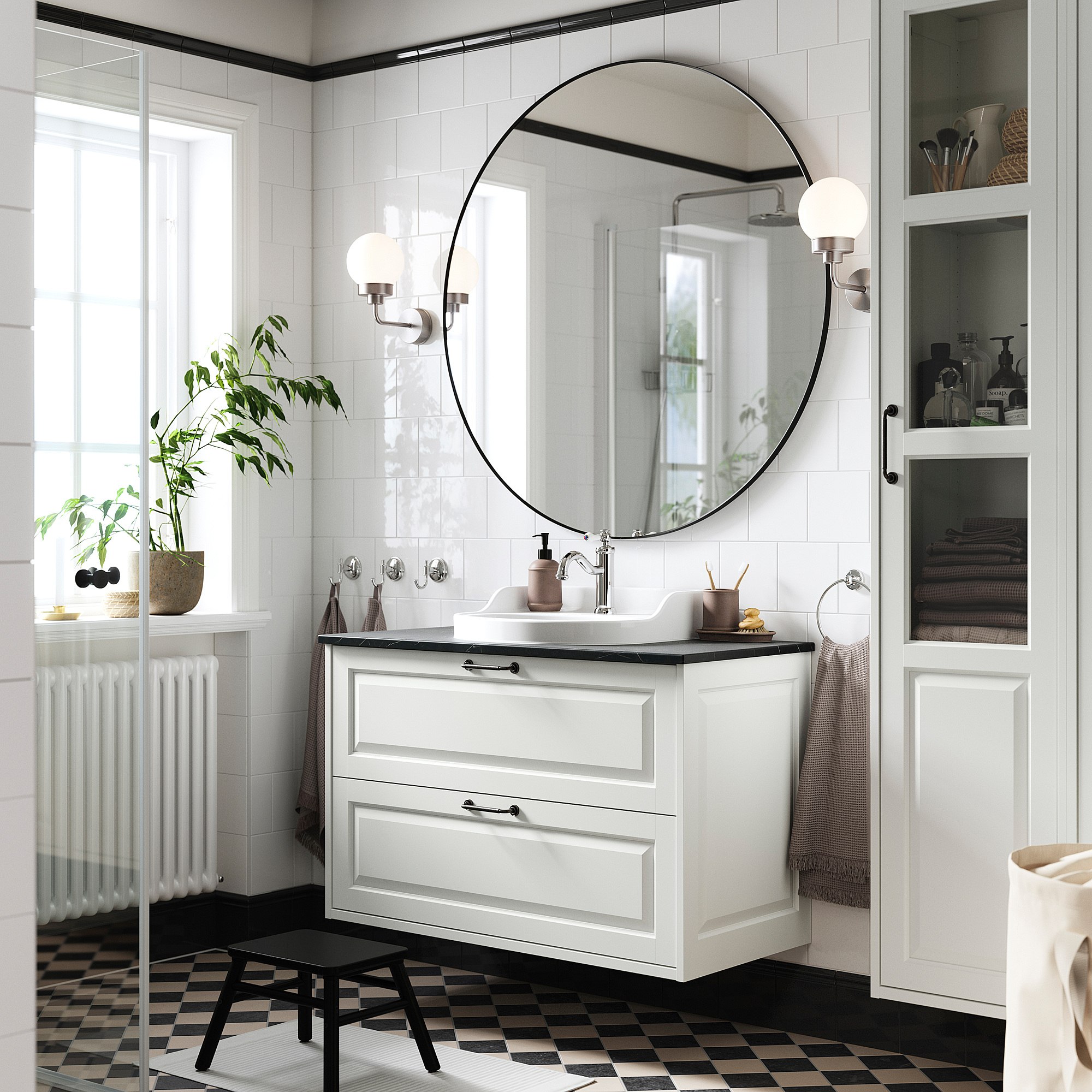 Modernes Badezimmer mit weißem Waschtisch TÄNNFORSEN, rundem Spiegel, schwarzem kariertem Boden und Topfpflanze.