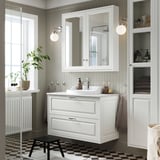 Modernes weißes Badezimmer mit TÄNNFORSEN-Waschtisch, großem Spiegel, schwarzem Hocker und schwarzer Toilette. Das Waschbecken ist zentral und von viel Stauraum umgeben.
