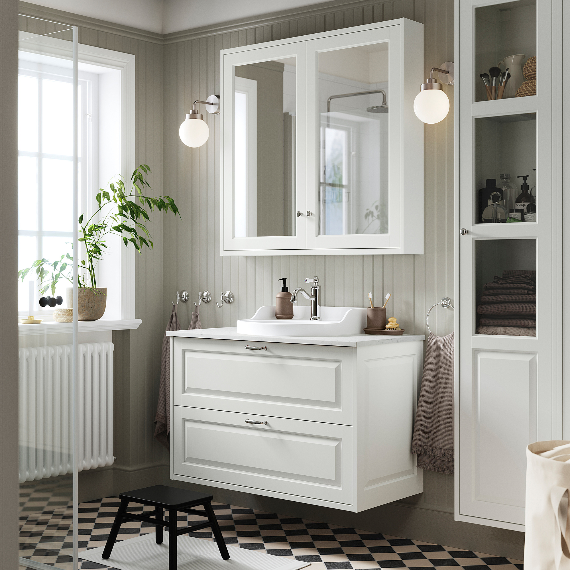 Modernes weißes Badezimmer mit TÄNNFORSEN-Waschtisch, großem Spiegel, schwarzem Hocker und schwarzer Toilette. Das Waschbecken ist zentral und von viel Stauraum umgeben.