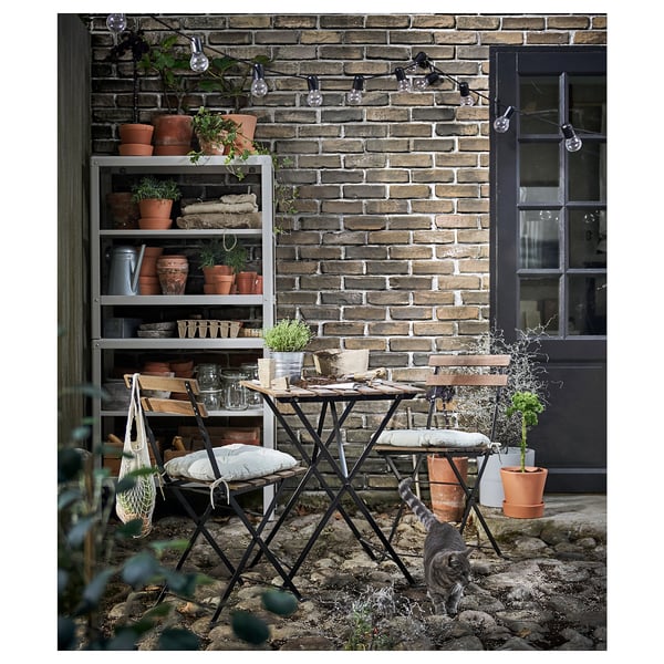 Kleine Terrasse mit Ziegelwand, Pflanzen, Tisch, Stuhl und Katze. Rustikal, gemütlich und einladend.