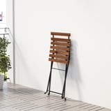 Klappstuhl aus Holz mit Rädern, der an einer Wand lehnt und für den Innen- und Außenbereich geeignet ist.