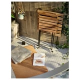 Außeneinrichtung mit Klapptisch aus Holz und Kissen auf gemusterter Matte.