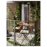 Kleiner Balkon mit Holztisch und weißen gepolsterten Stühlen, umgeben von üppigen grünen Pflanzen.