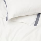 Strahlend weiße Bettwäsche mit elegantem blauem Besatz, der hochwertige Materialien und sorgfältige Verarbeitung präsentiert.