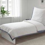 Weißes TÅTELSMYGARE-Bettdeckenset auf kleinem Bett, frische Bio-Baumwolle, blauer Besatz, gemütliches, minimalistisches Design.