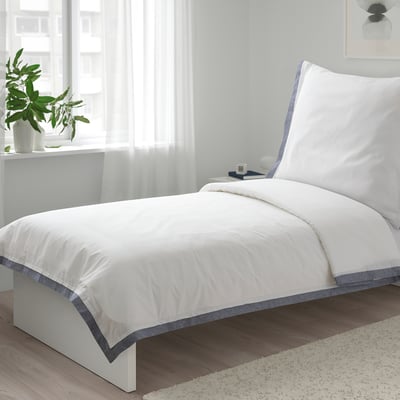 Weißes TÅTELSMYGARE-Bettdeckenset auf kleinem Bett, frische Bio-Baumwolle, blauer Besatz, gemütliches, minimalistisches Design.