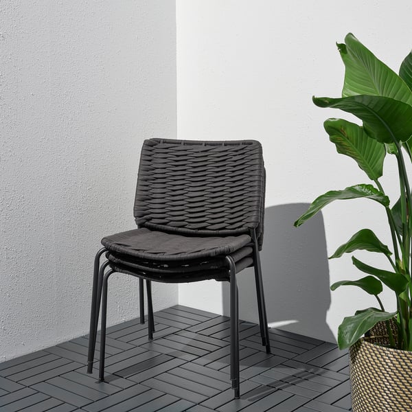 Moderner Korbsessel mit geschlungenem Sitz auf dunklem Deck, Rückseite mit weißer Wand und grüner Pflanze.