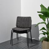 Moderner Korbsessel mit geschlungenem Sitz auf dunklem Deck, Rückseite mit weißer Wand und grüner Pflanze.
