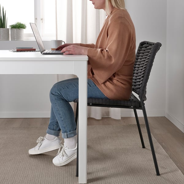 Frau sitzt auf einem schwarzen Seilsessel und arbeitet mit einem Laptop an einem weißen Schreibtisch.