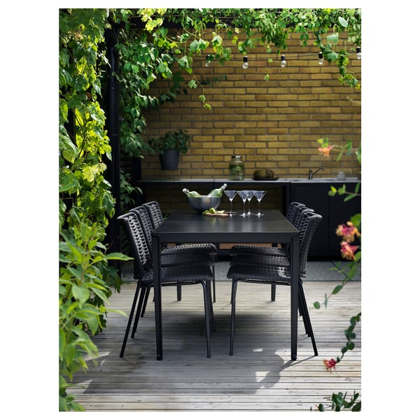 Moderne Außenterrasse mit schwarzem TEGELÖN-Tisch und Stühlen, Backsteinwand, Pflanzen.