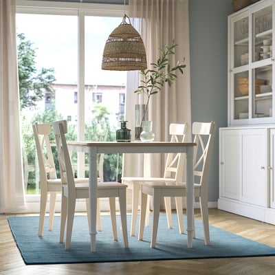 Modernes Esszimmer mit TIDTABELL-Tisch, vier Stühlen, graublauem Teppich. Pendelleuchte, weißer Schrank mit Geschirr, große Fenster.