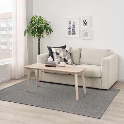 Modernes Wohnzimmer mit hellgrauem TIPHEDE-Teppich, weißem Sofa, Couchtisch aus Holz und Pflanze. Kunst an der Wand.