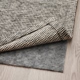 Grau karierter Teppich mit Filzunterlage auf Holzboden.